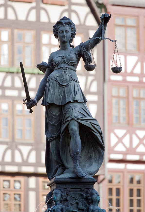 Teisingumo deivė vaizduojama akla, kairėje laikanti svarstykles, dešinėje - kalaviją (teisingumui įgyvendinti)