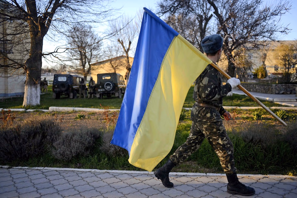 Ukrainiečių karys neša Ukrainos vėliavą Belbeko karinių oro pajėgų bazėje. EPA-Eltos nuotr.