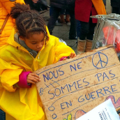 Vaiko rankose laikomas plakatas su užrašu „Mes nesame kare“.